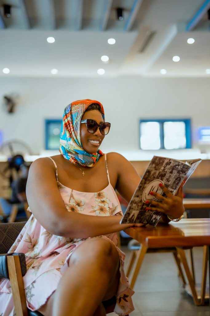 Smiling woman in headscarf reads a magazine inside a modern room, capturing a moment of relaxation.